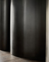 Dark grey cylindrical table base with brushed metal finish on wooden floor