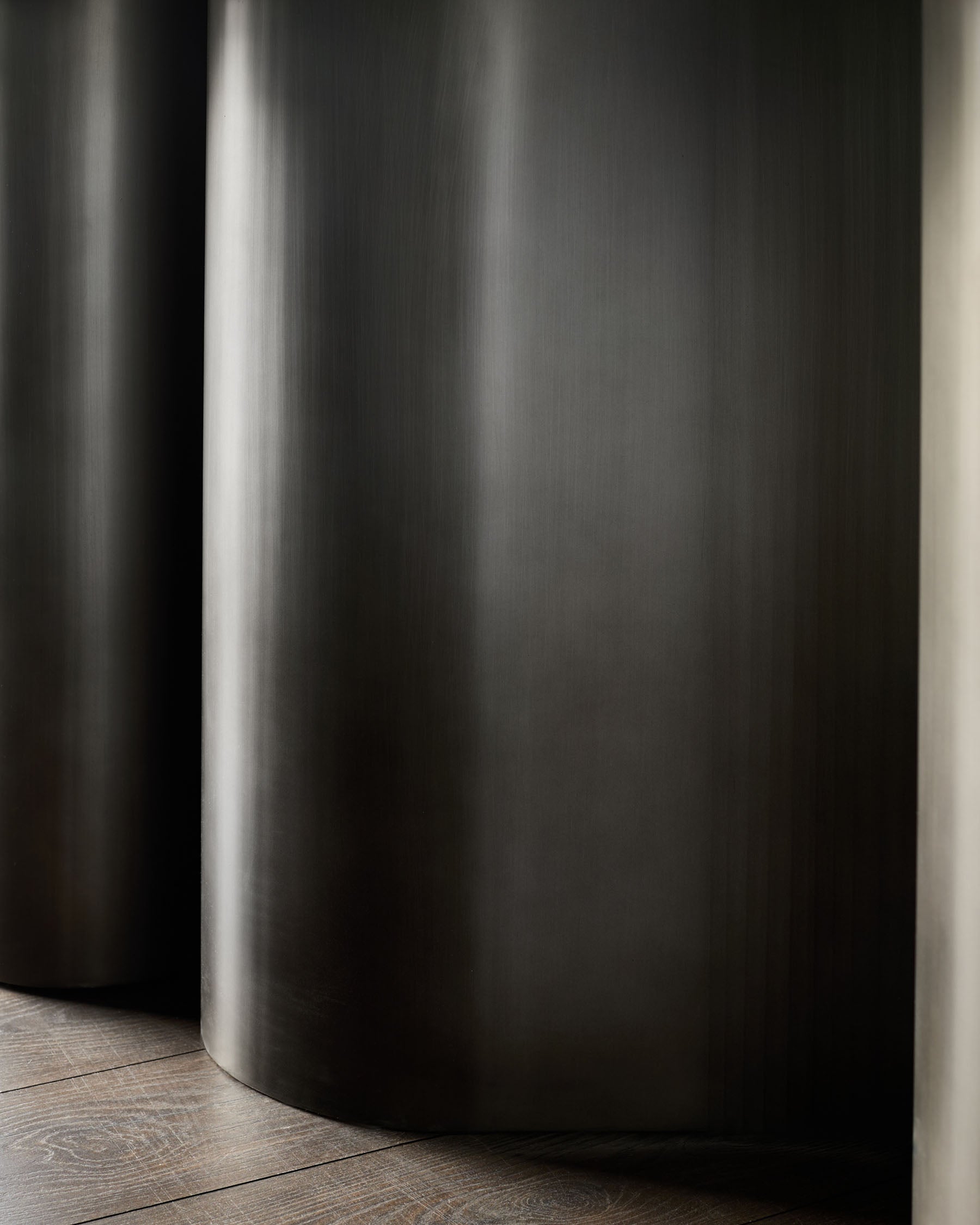 Dark grey cylindrical table base with brushed metal finish on wooden floor