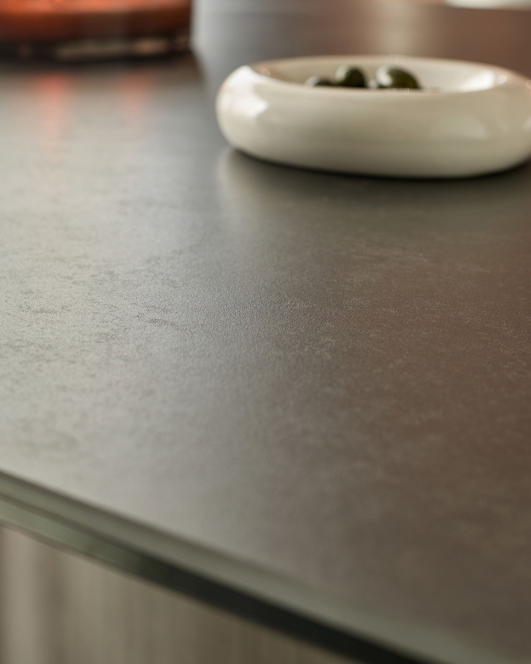 Close-up of dark grey ceramic dining table surface with white bowl and utensils.