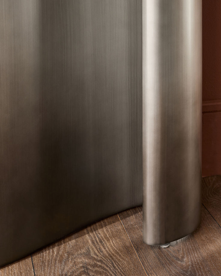 Carlo console table in dark grey ceramic with brushed metal cylindrical support leg on wood flooring.