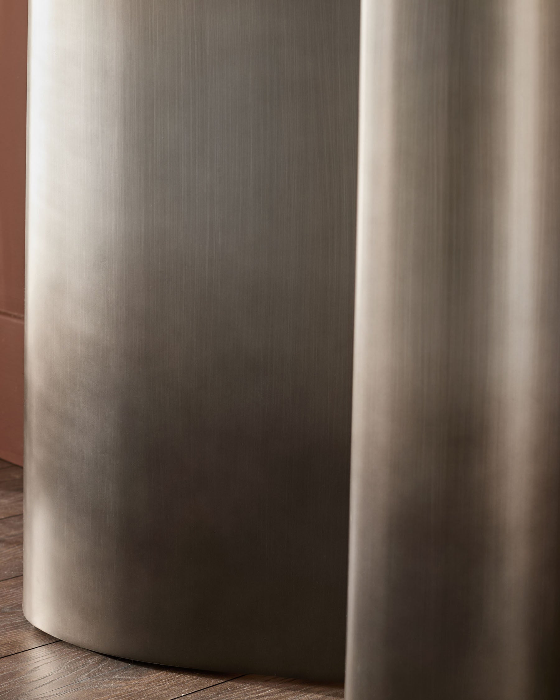 Carlo console table in dark grey ceramic, cylindrical base detail, close-up side view on wooden floor.