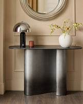 Carlo console table in dark grey ceramic with curved base, styled with chrome lamp and white vase in contemporary entryway setting.