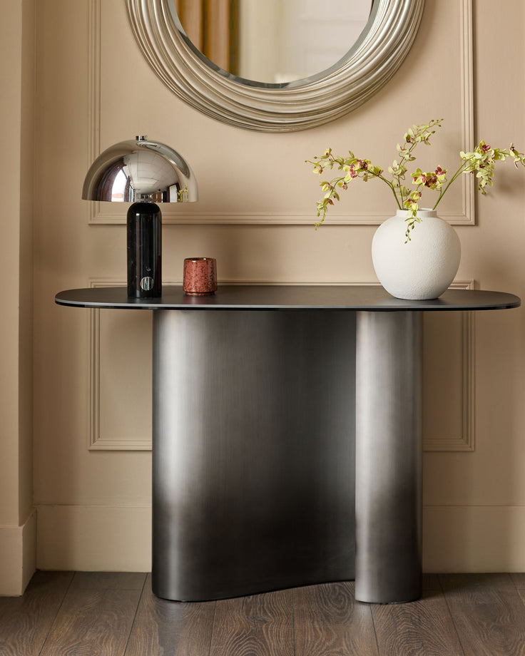 Carlo console table in dark grey ceramic with curved base, styled with chrome lamp and white vase in contemporary entryway setting.