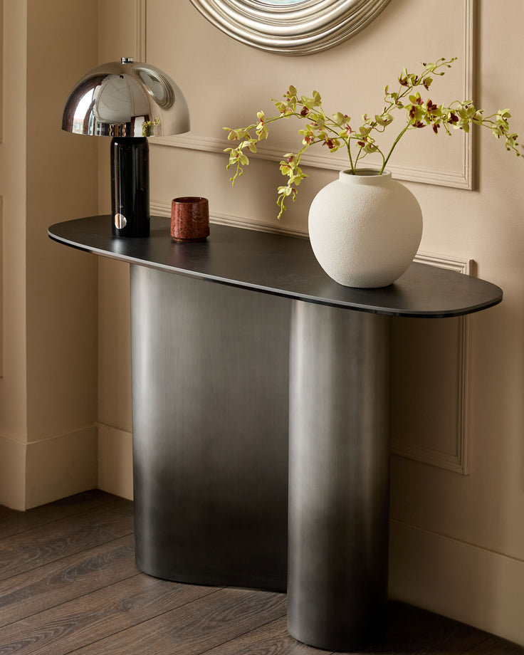 Carlo console table in dark grey ceramic with black top, styled with lamp, vase, and orchids in modern entryway setting.