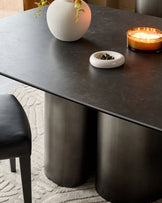 Carlo 8-seater dining table in dark grey ceramic with cylindrical base, styled with white vase, candle, and bowl.
