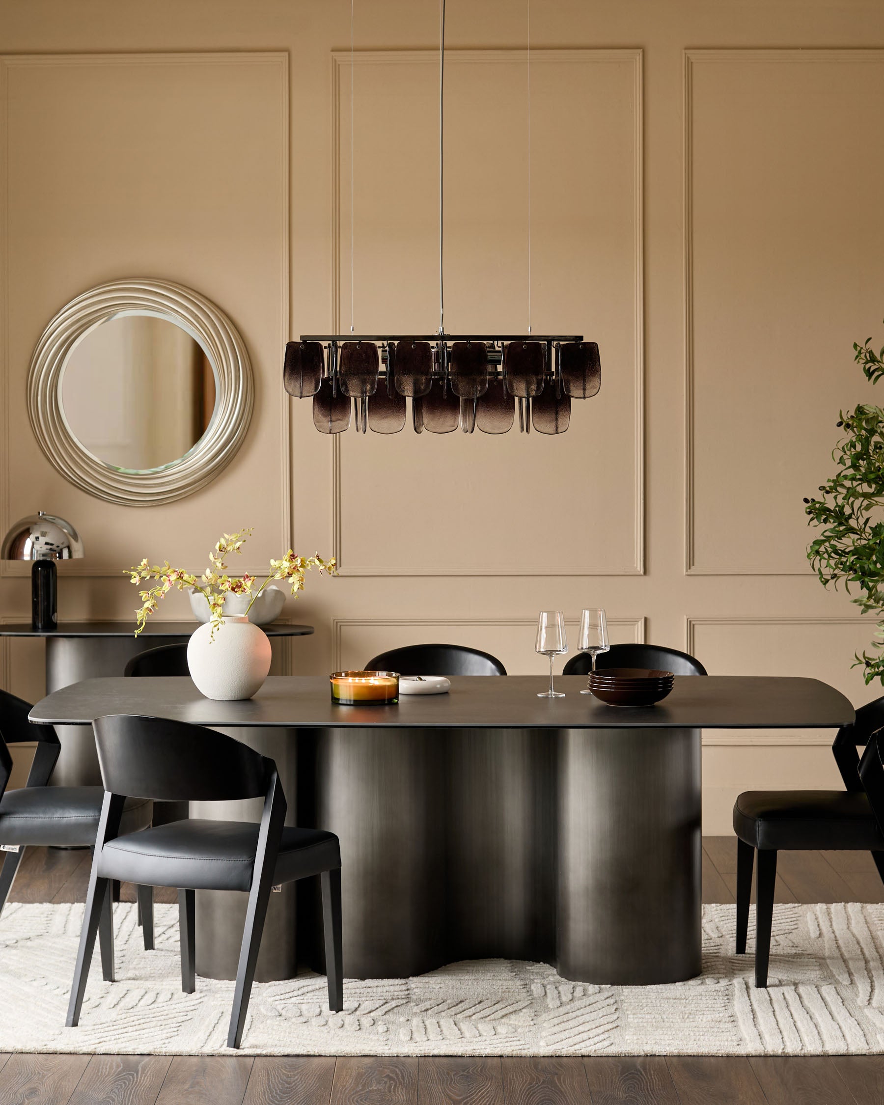 Carlo 8-seater dining table in dark grey ceramic with curved cylindrical base, styled with black chairs and pendant lighting.