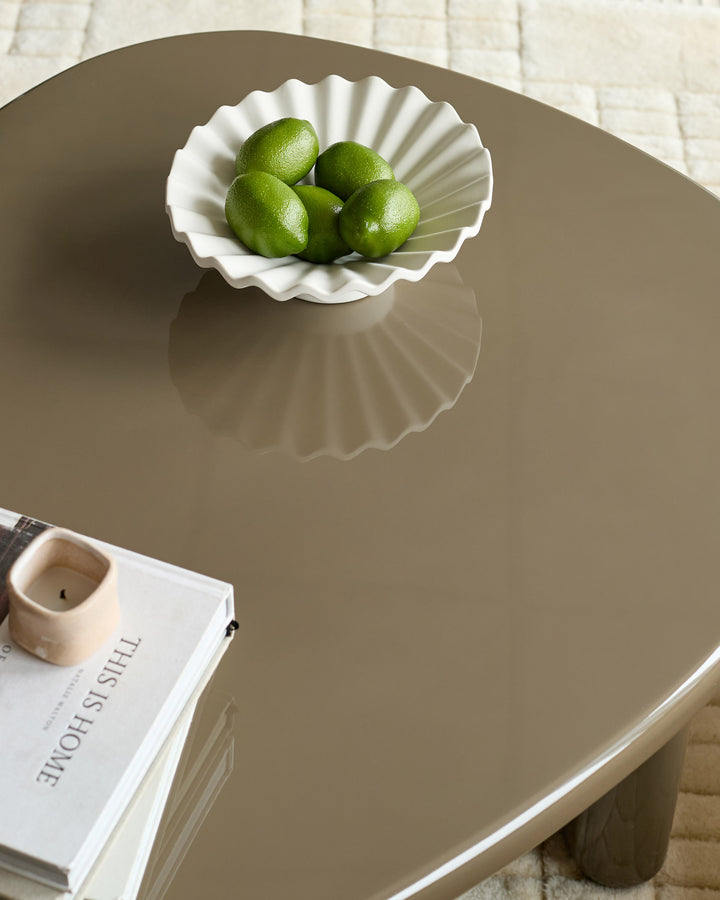 Carmela gloss olive-green coffee table with curved edges, styled with white shell bowl of limes and magazine.