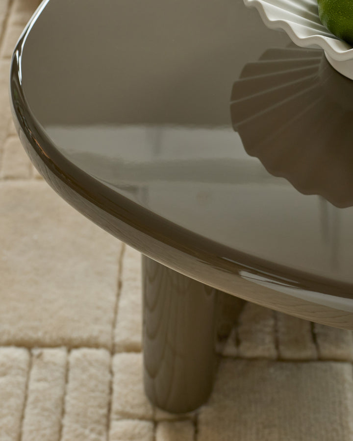 Carmela coffee table in gloss olive green, showing curved edge detail and wooden pedestal base on cream tile floor.