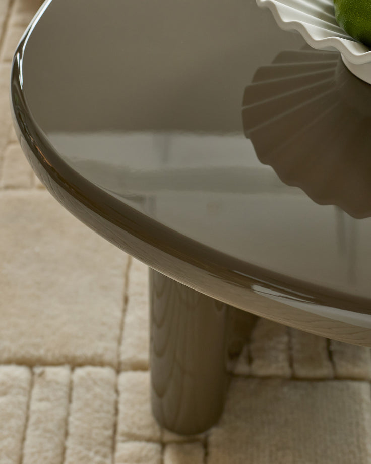 Carmela coffee table in gloss olive green, showing curved edge detail and wooden pedestal base on cream tile floor.