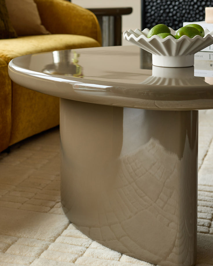 Carmela coffee table in gloss olive green with round top and sculptural pedestal base, styled in modern living room.