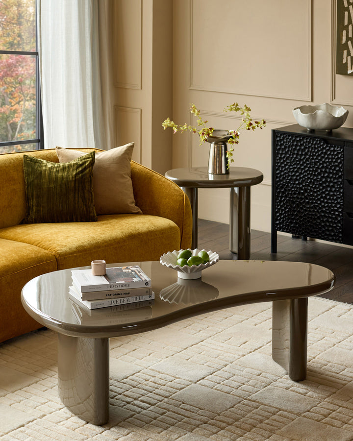 Gloss olive green Carmela coffee table with organic curved shape and cylindrical base in a modern living room setting.