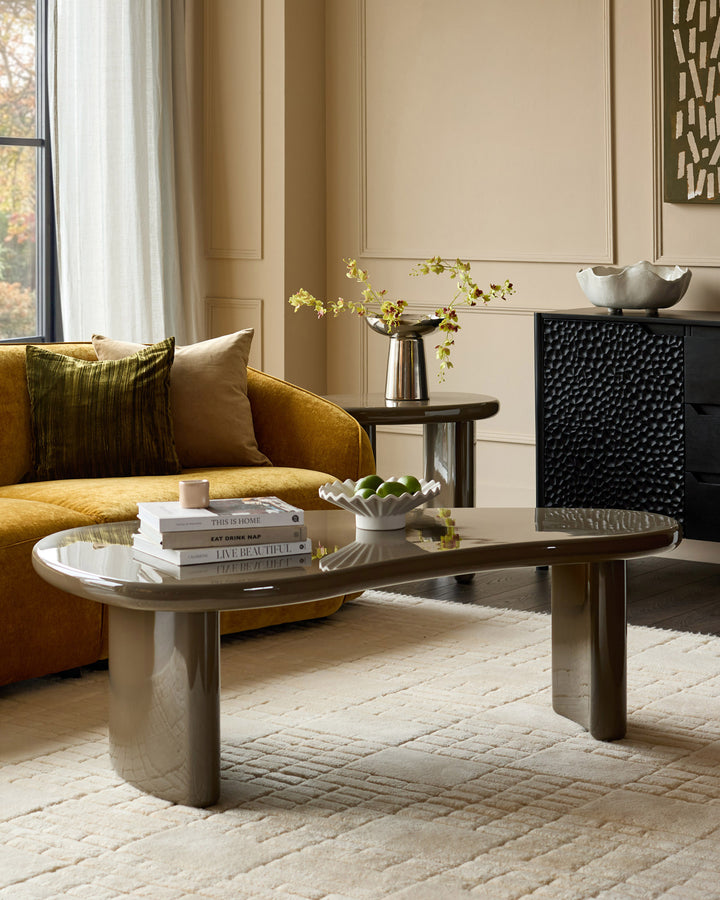 Carmela Coffee Table in gloss olive green, oval shape with rounded cylindrical base, displayed in a modern living room setting.