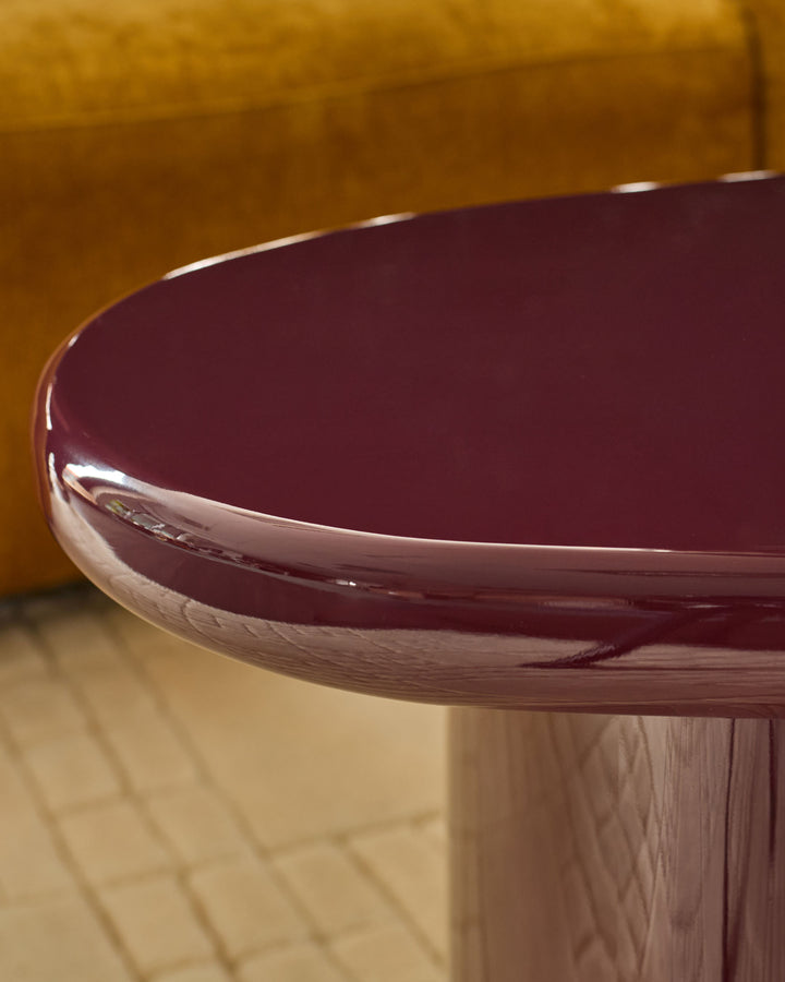 Gloss plum round coffee table with natural wood base, detail view of curved tabletop edge.
