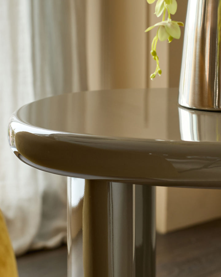 Carmela side table in gloss olive green, shown at an angle highlighting its curved tabletop and cylindrical pedestal base.