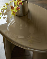 Gloss olive-green side table with curved cylindrical base and rounded tabletop, styled with yellow orchids in vase.