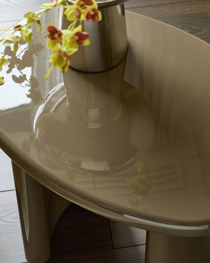 Gloss olive-green side table with curved cylindrical base and rounded tabletop, styled with yellow orchids in vase.