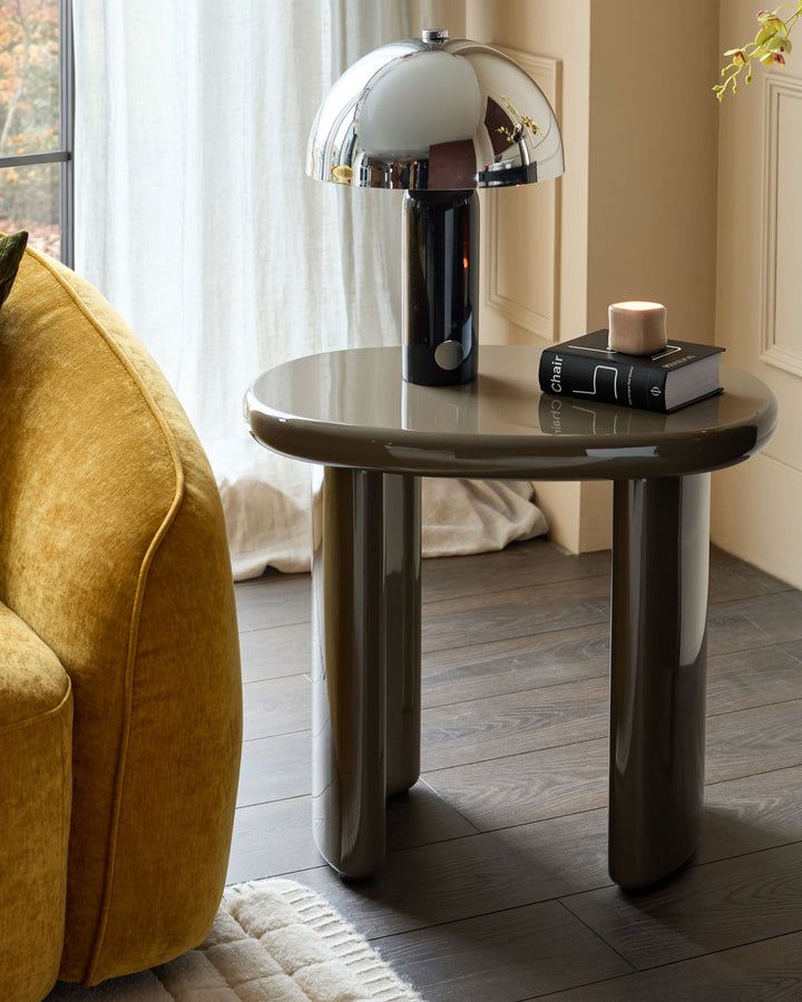 Carmela side table in gloss olive green with rounded cylindrical base, styled with chrome mushroom lamp and book decor.