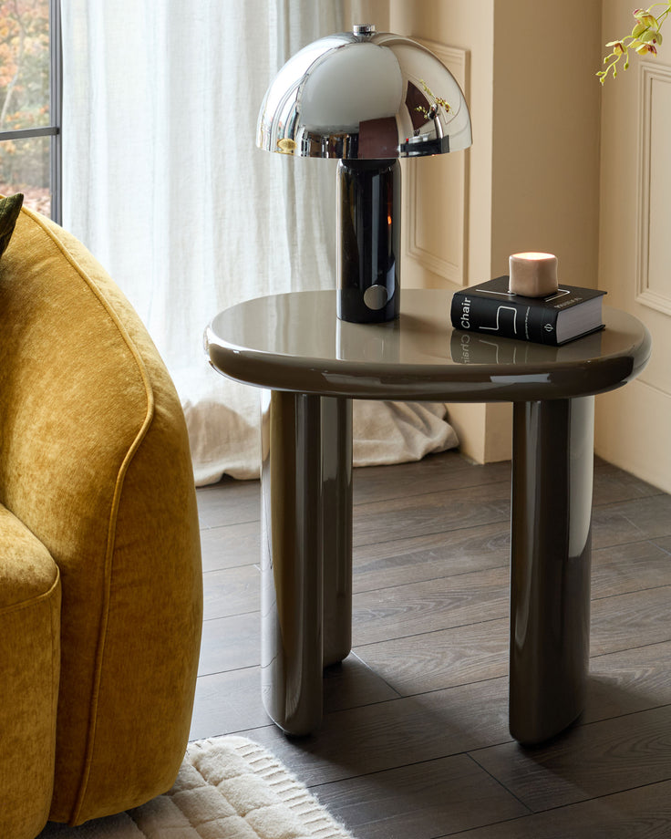 Carmela side table in gloss olive green with rounded cylindrical base, styled with chrome mushroom lamp and book decor.