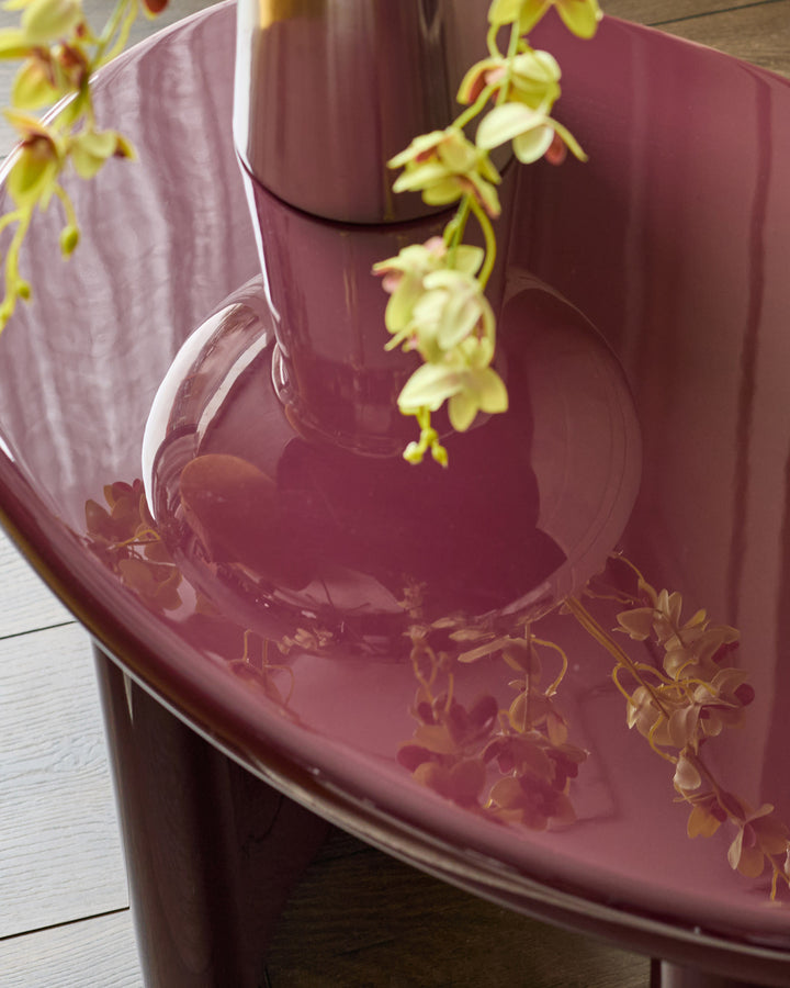 Gloss plum side table with yellow orchid flowers cascading over curved edge, viewed from above at angle.