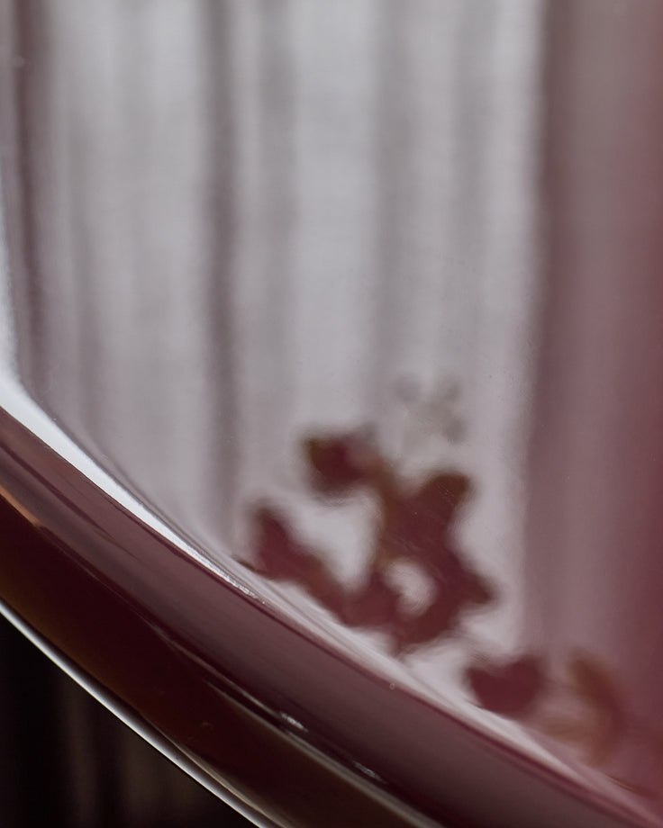Carmela side table in gloss plum, shown at an angle highlighting its curved edge and reflective finish against a light background.