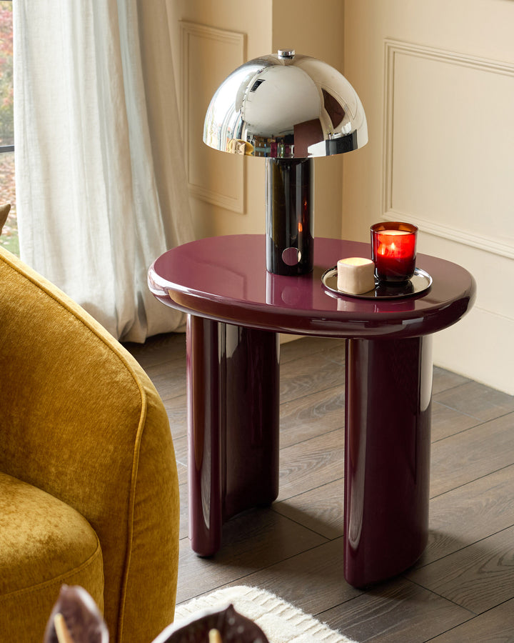 Gloss plum side table with curved cylindrical base, styled with chrome mushroom lamp and red candle in modern living room.