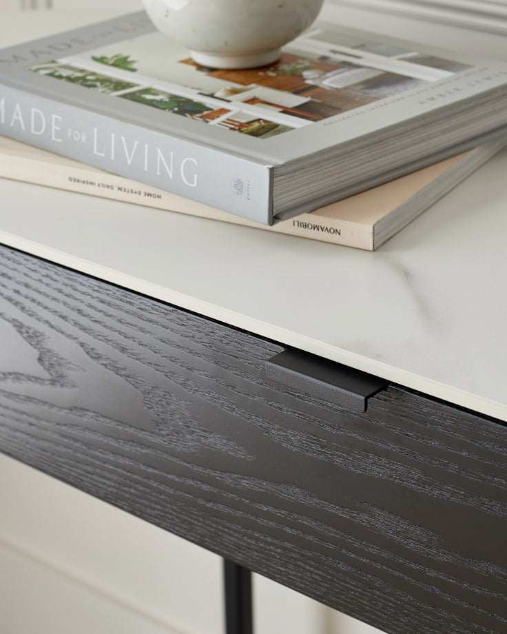 Black wood-grain console table with white top surface, styled with stacked books and a white ceramic bowl.