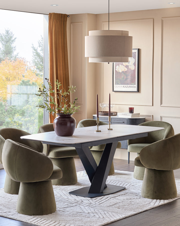 Carter extending dining table in natural ceramic with black V-shaped base, seated with olive green chairs.