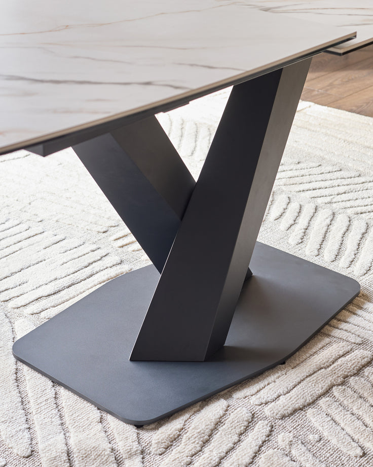 Carter extending dining table with black V-shaped pedestal base and marble-effect ceramic top, side view.