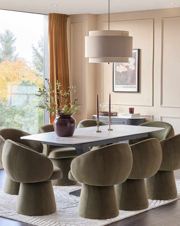 Carter extending dining table in natural ceramic with black base, shown extended with six sage green upholstered chairs in modern dining room.