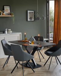 A dining area with a dark table and four modern grey chairs with black legs, illuminated by candles.