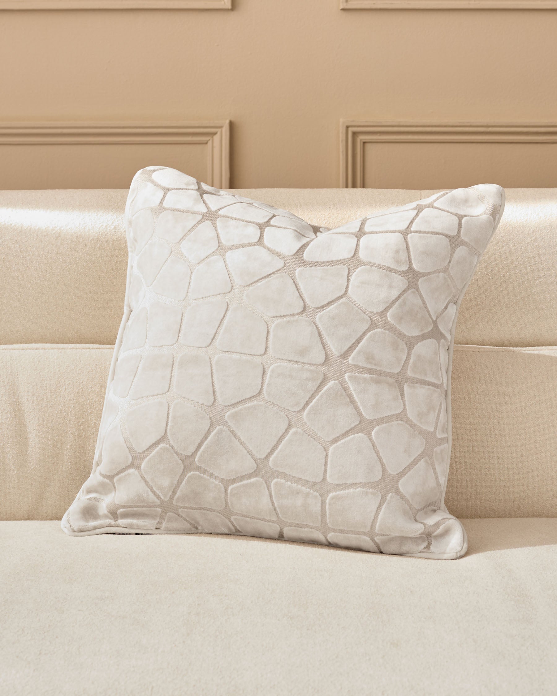 Cassidy Cushion in ivory with quilted geometric pattern, displayed on a beige sofa against paneled wall.