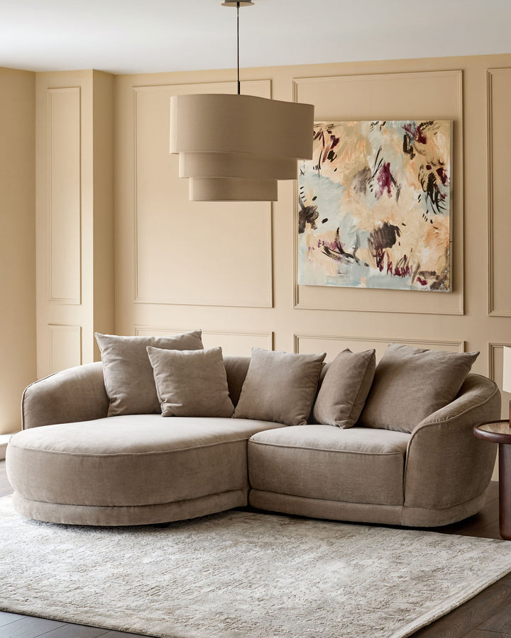 Mink fabric left-hand corner chaise sofa with curved arms and five scatter cushions in a neutral living room setting.