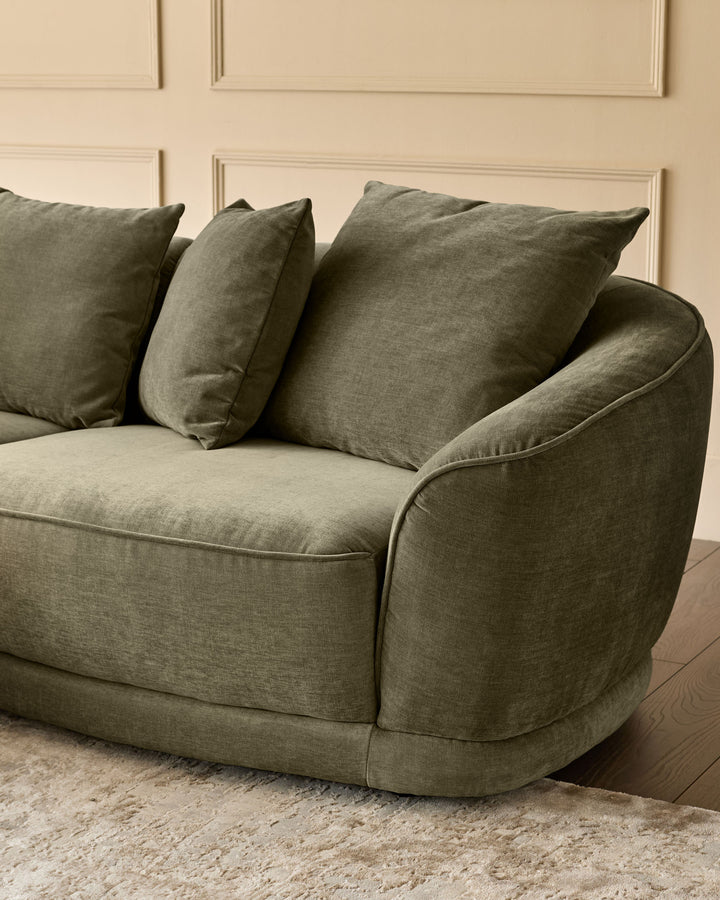 Caspian right-hand corner chaise sofa in olive green fabric, shown from side angle with decorative pillows, on beige rug.