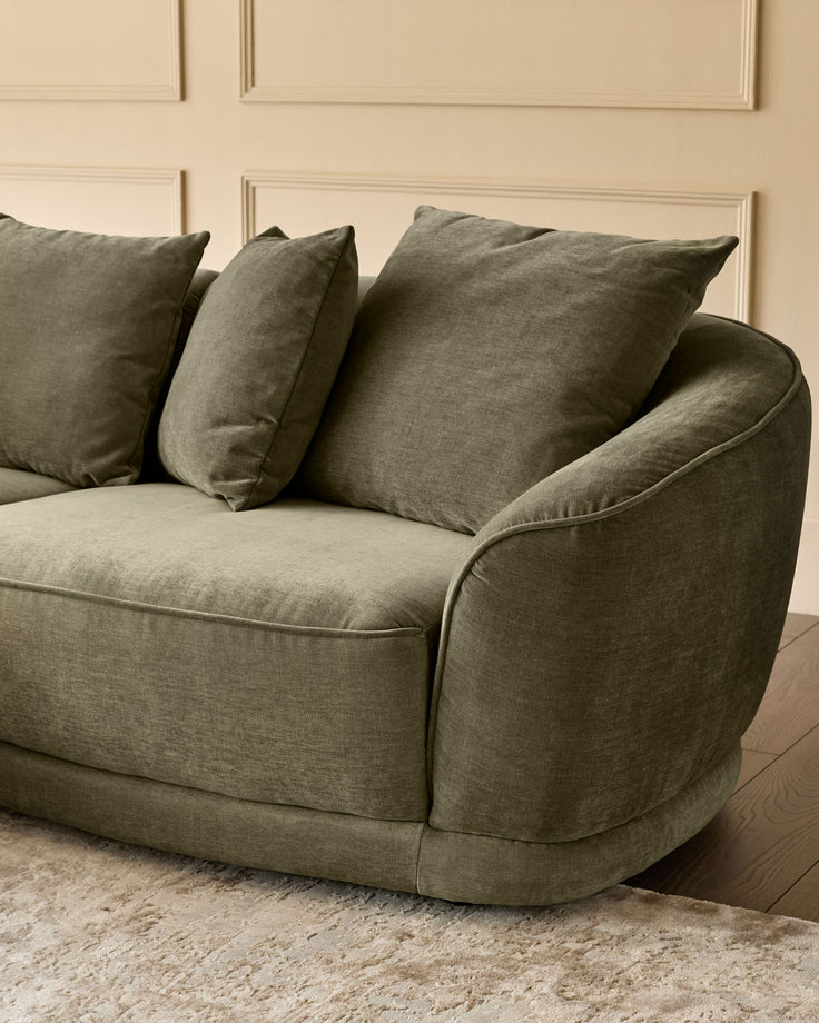 Caspian right-hand corner chaise sofa in olive green fabric, shown from side angle with decorative pillows, on beige rug.
