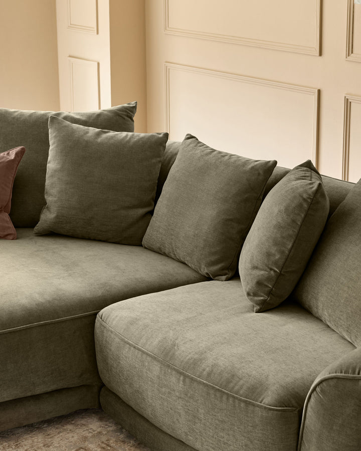 Caspian single module fabric sofa in olive green with matching throw pillows, angled view against paneled wall.