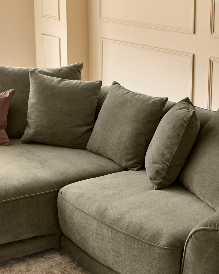Caspian single module fabric sofa in olive green with matching throw pillows, angled view against paneled wall.