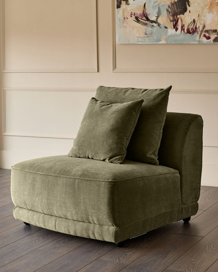 Caspian single module fabric chair in olive green with decorative pillows, angled side view on dark wood floor.
