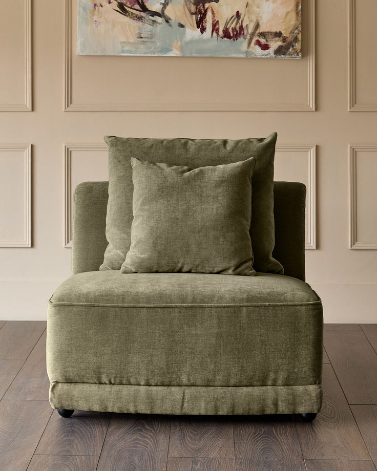 Caspian single-module fabric chair in olive green with matching throw pillows, displayed against a beige paneled wall.