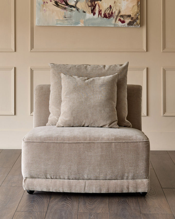 Mink fabric single-seat module with matching throw pillows, wooden legs, against paneled wall backdrop.