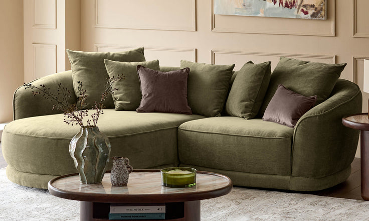 Olive-green curved sectional sofa with plush cushions and decorative pillows in a modern living room setting.