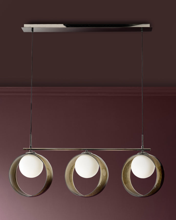 Chloe 3-pendant light with green glass spheres suspended from a linear chrome rail against a burgundy wall.
