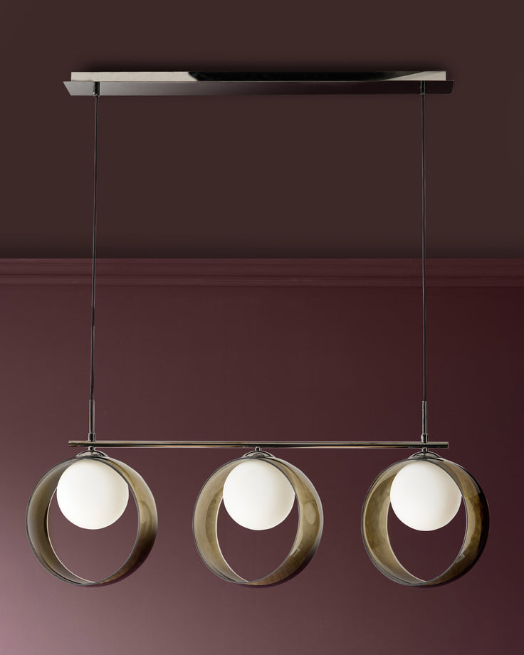 Chloe 3-pendant light with green glass spheres suspended from a linear chrome rail against a burgundy wall.