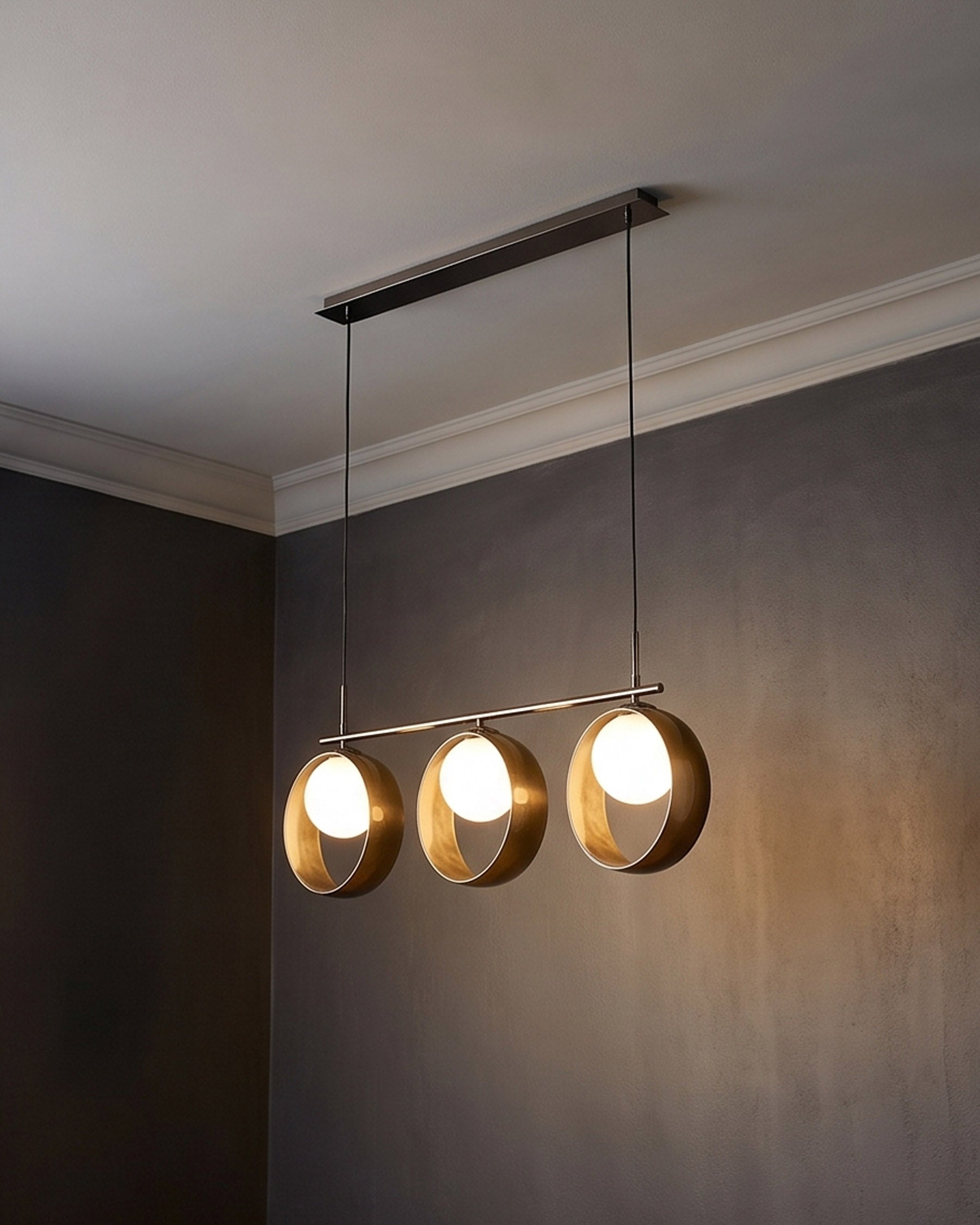 Chloe 3-pendant light with brass-finished spherical shades suspended from dark metal rod against neutral wall.
