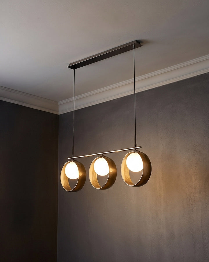 Chloe 3-pendant light with brass-finished spherical shades suspended from dark metal rod against neutral wall.