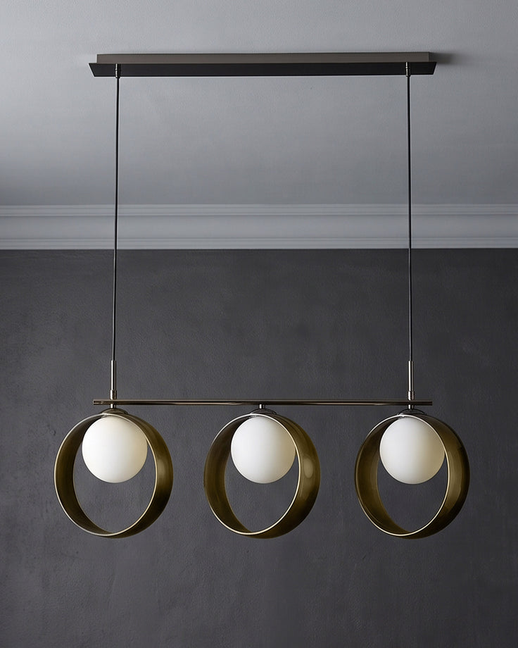 Chloe 3-pendant light with green metal rings and white spherical glass shades, suspended from dark ceiling fixture.
