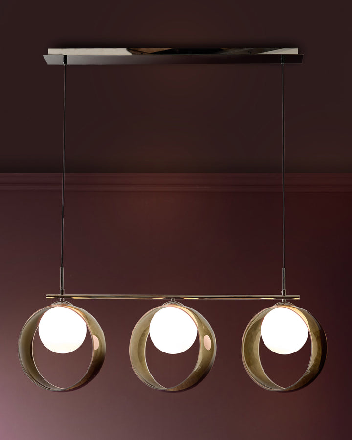 Chloe 3-pendant light with green glass spheres suspended from brass rod and ceiling fixture against burgundy wall.