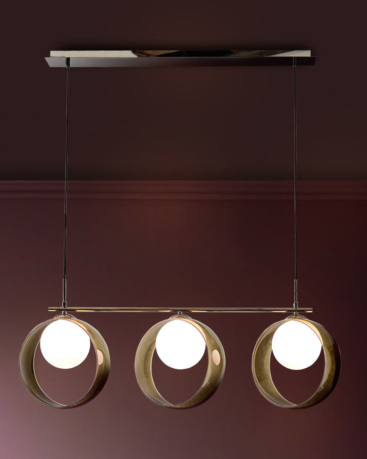 Chloe 3-pendant light with green glass spheres suspended from brass rod and ceiling fixture against burgundy wall.