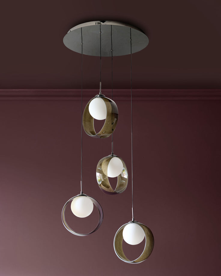 Chloe 4-pendant light with green glass spheres and brass orbital frames suspended from a grey ceiling canopy against a burgundy wall.