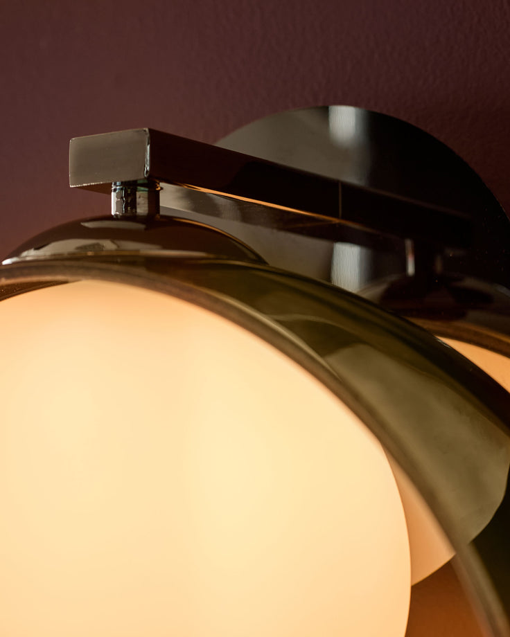 Chloe wall light with curved green metal arm and illuminated frosted glass globe shade, close-up detail view.