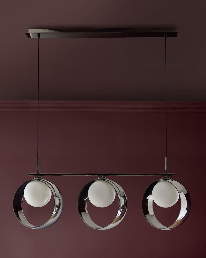 Chloe 3-pendant light with chrome frame and frosted glass spheres suspended from black bar mount against burgundy wall.